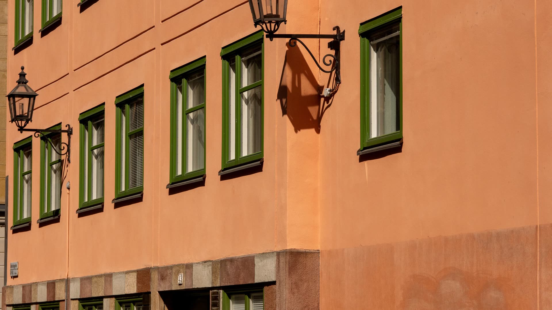 En port i en orange putsfasad med gröna fönsterbågar, smidda gatlyktor och kullersten framför.