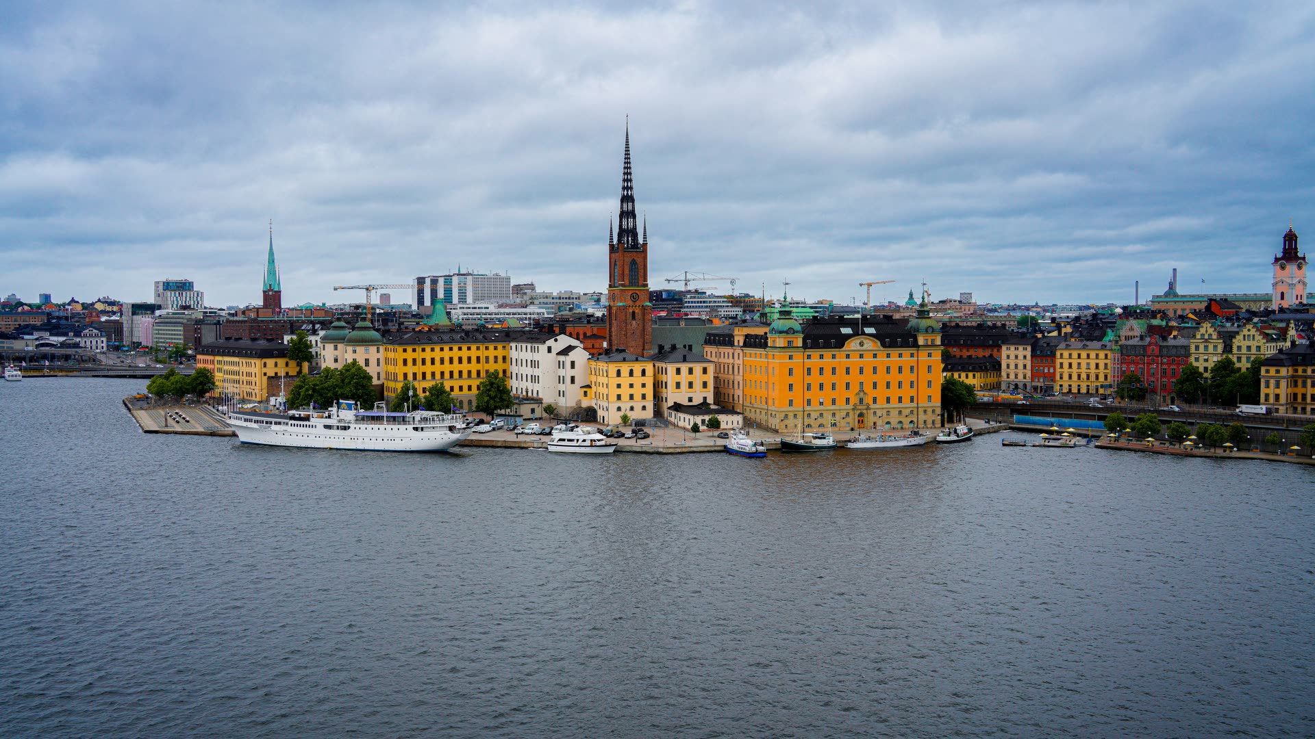 Stockholm sett över Riddarfjärden en mulen dag: Riddarholmens kyrka, Gamla stans tak och Norrmalms hus bakom, med öppet vatten i förgrunden.
