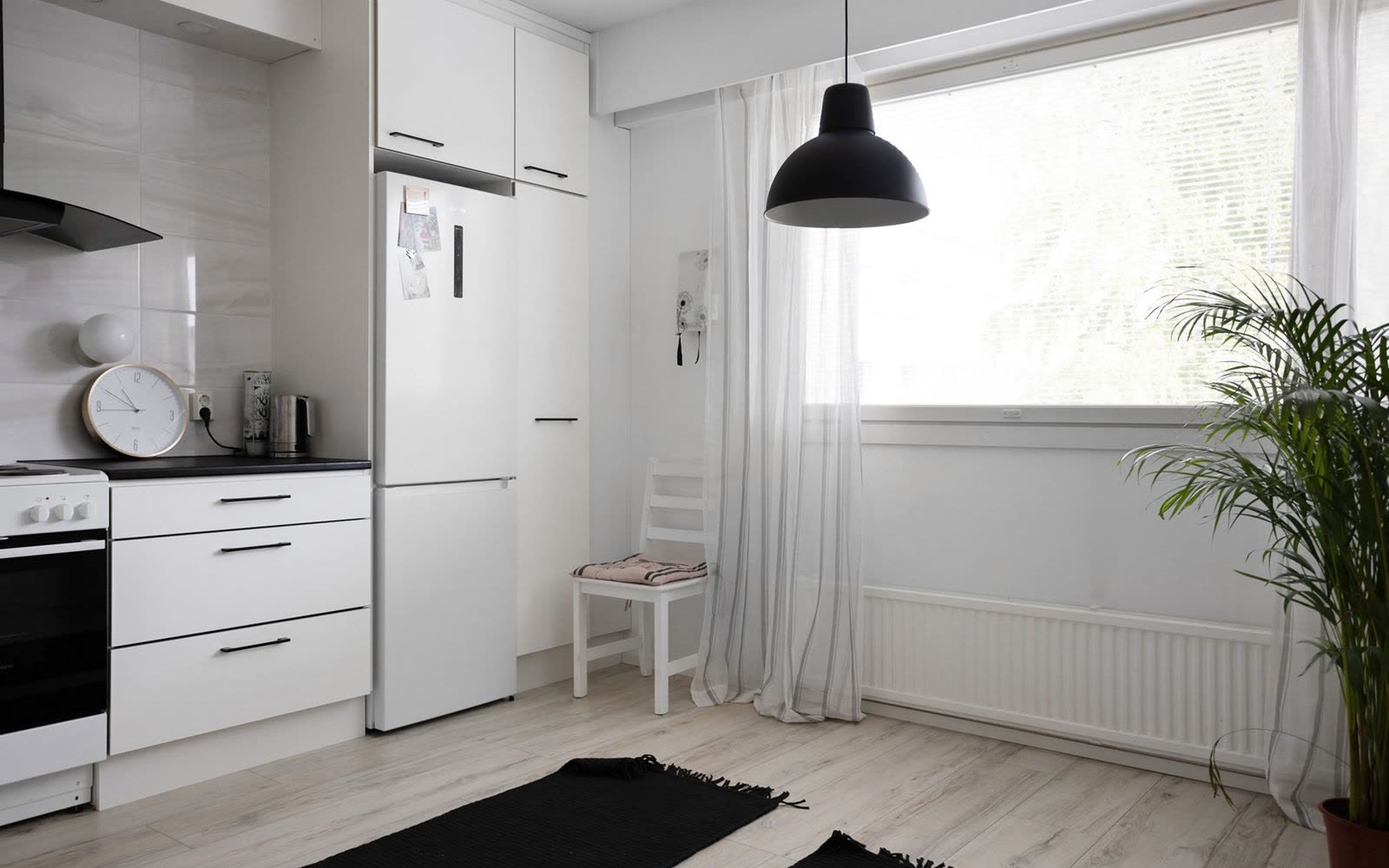 Vitt kök med stort fönster, radiator och trasmattor