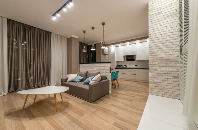 Öppen planlösning med soffa, kök och tegelvägg