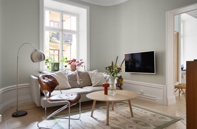 Grönt vardagsrum med soffa, tv och gammalt trägolv