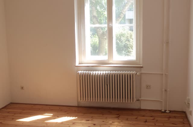 Tomt rum med furugolv och radiator under valvfönster