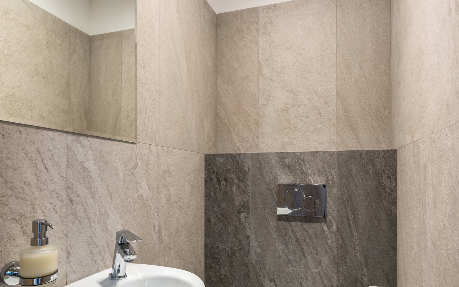Kompakt gäst-wc med gråa stenplattor och vägghängd toalett