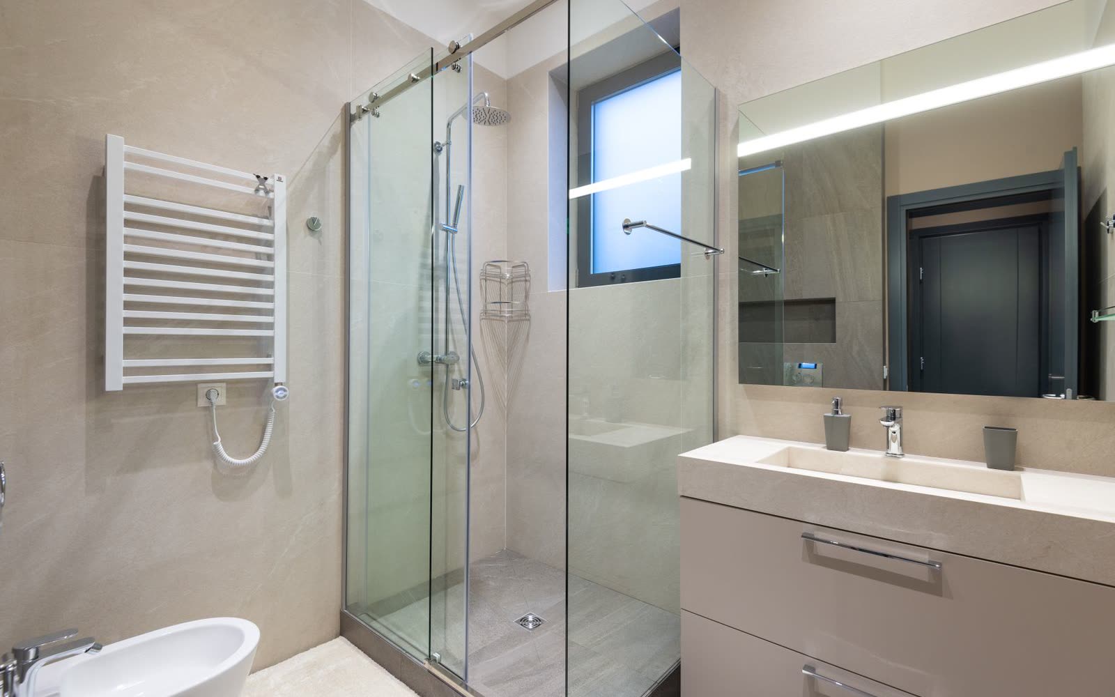 Beige stenbadrum med glasdusch och upplyst spegel