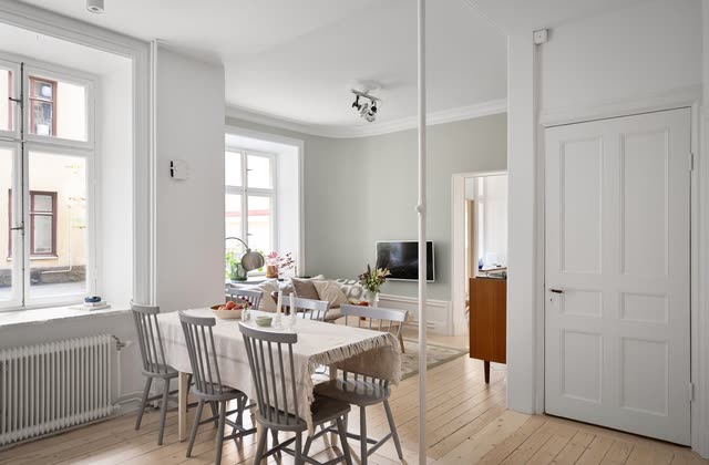 Öppen planlösning med matbord, pinnstolar och vardagsrum bortom