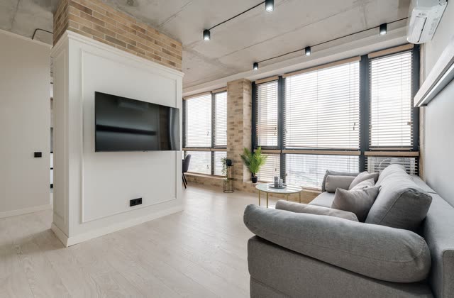 Loftlägenhet med tv-vägg, persienner och grå soffa