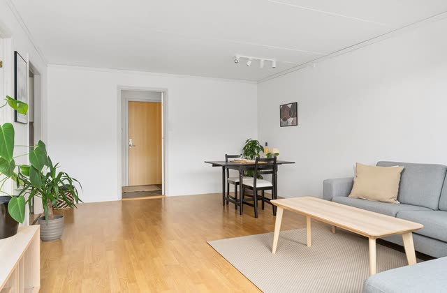 Avskalat vardagsrum med matplats, soffa och ljust laminatgolv