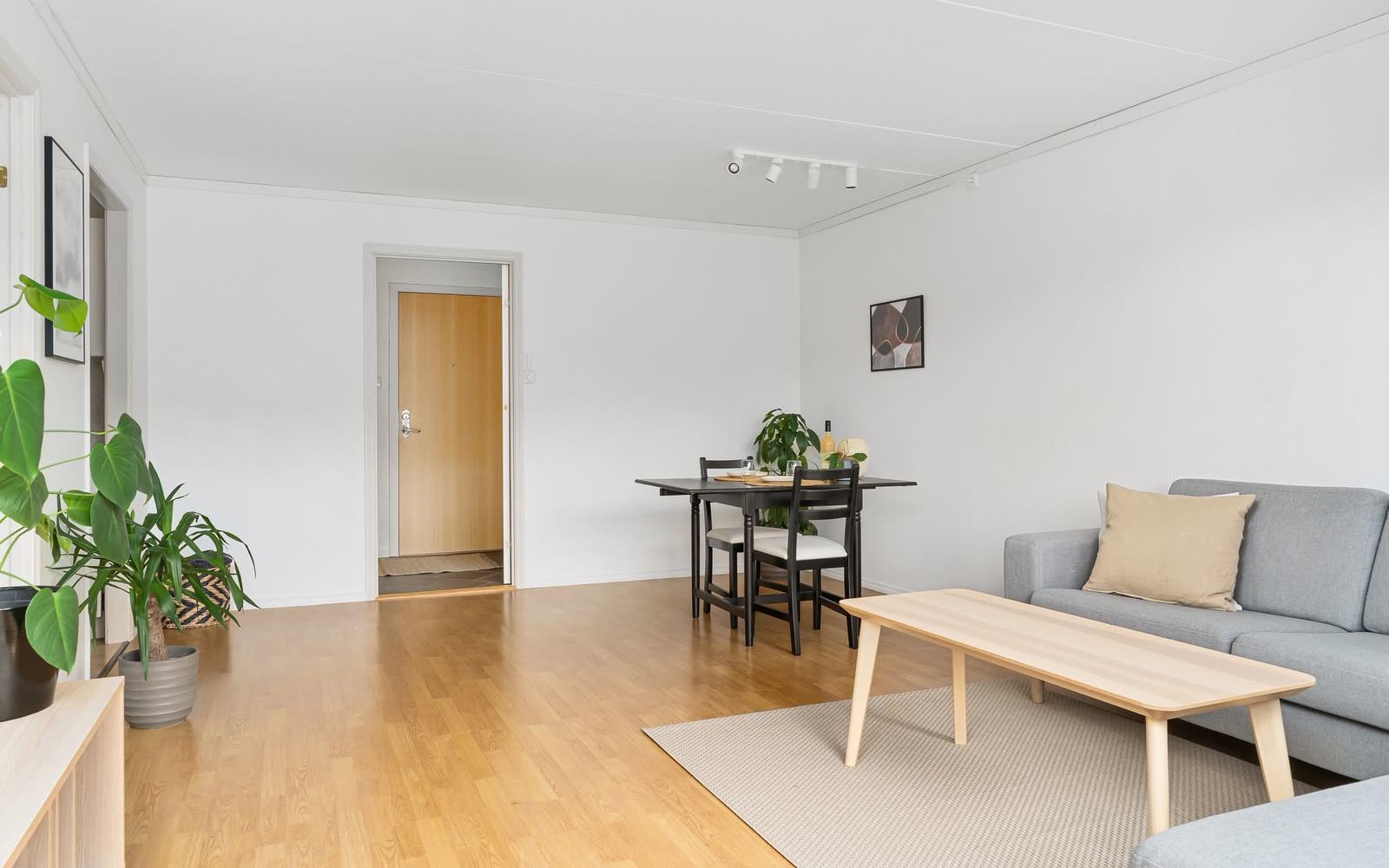 Avskalat vardagsrum med matplats, soffa och ljust laminatgolv