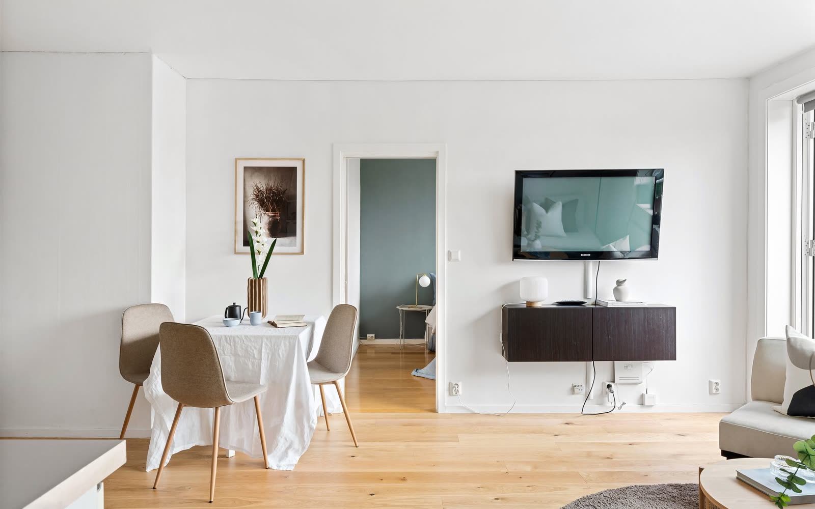Ljus vägg med matplats, tv och sovrum genom dörren